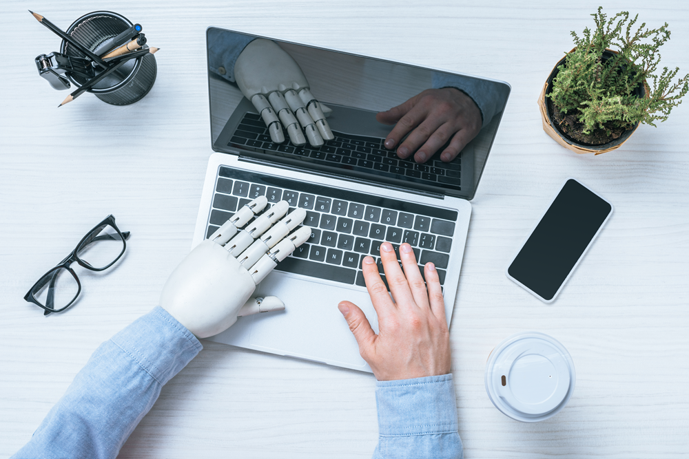 Robot hand and human typing on laptop
